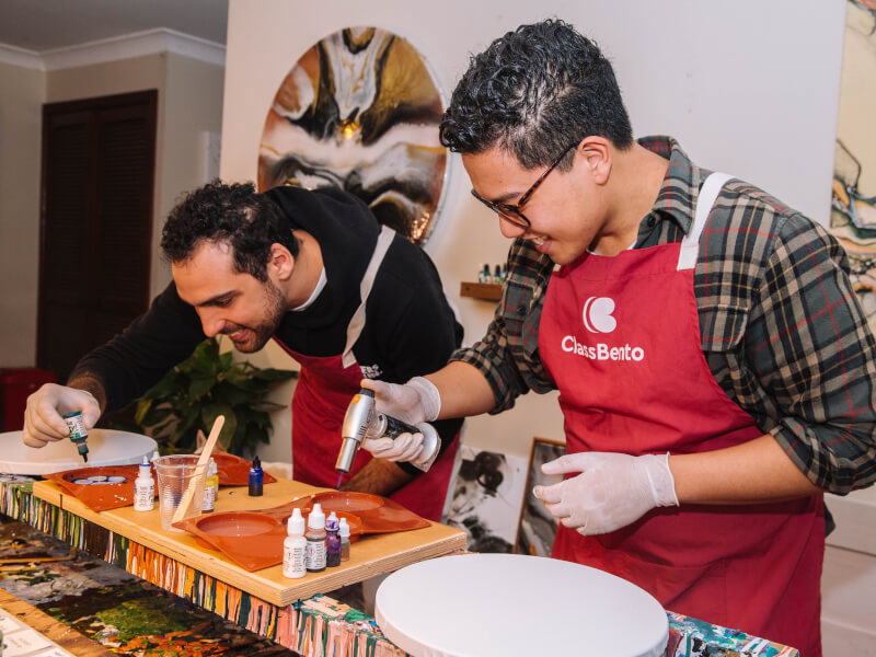 Two men wearing aprons at a fluid art class.
